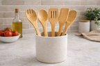 Set of wooden utensils in a container on a kitchen counter with tomatoes and oil in the background.