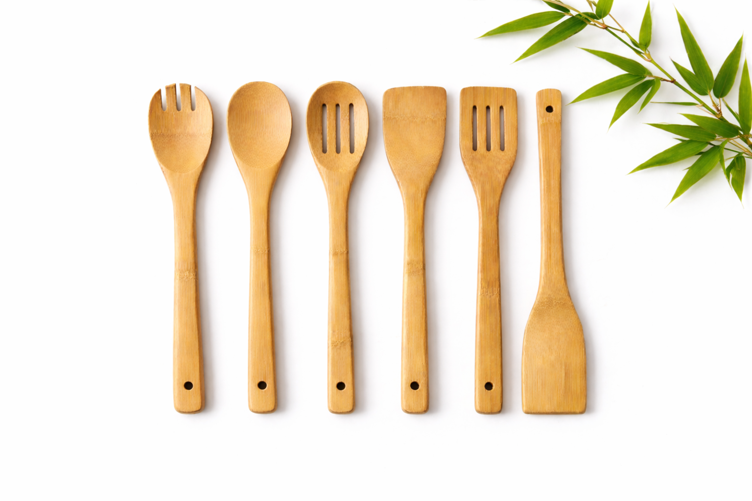 Set of wooden kitchen utensils on a white background with green leaves.