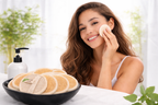 Woman applying facial mask with a bowl of loofah sponges and a bottle in the background