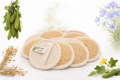 Set of natural sponges with a brand label, surrounded by greenery on a light background