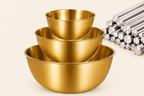 Set of three gold metal mixing bowls on a beige background
