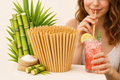 Woman drinking a cocktail with a lemon wedge, surrounded by bamboo straws and plants.