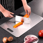 Person slicing carrots on a stainless steel cutting board with a knife.